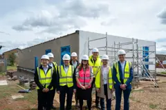 Councillors and partners are standing in front of the new building which is still under construction.  Everyone is wearing hard hat and hi-vis jackets 