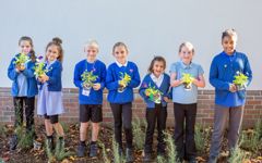 pupils are smiling and holding up the wildflowers they are about to plant 