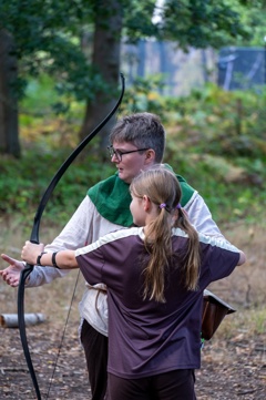 A young girl is being shown how to use a bow and arrow 