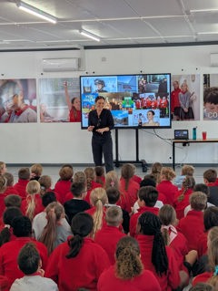Vicky McClure  is standing in a school assemble with pupils sat on the floor listening and watching her 