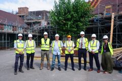 Partners are lined up wearing hi-vis and hard hats.  In the background is the school which is covered in scaffolding 