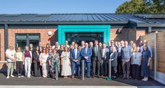 A large group of people are standing outside the building's main entrance for a 'group' photo