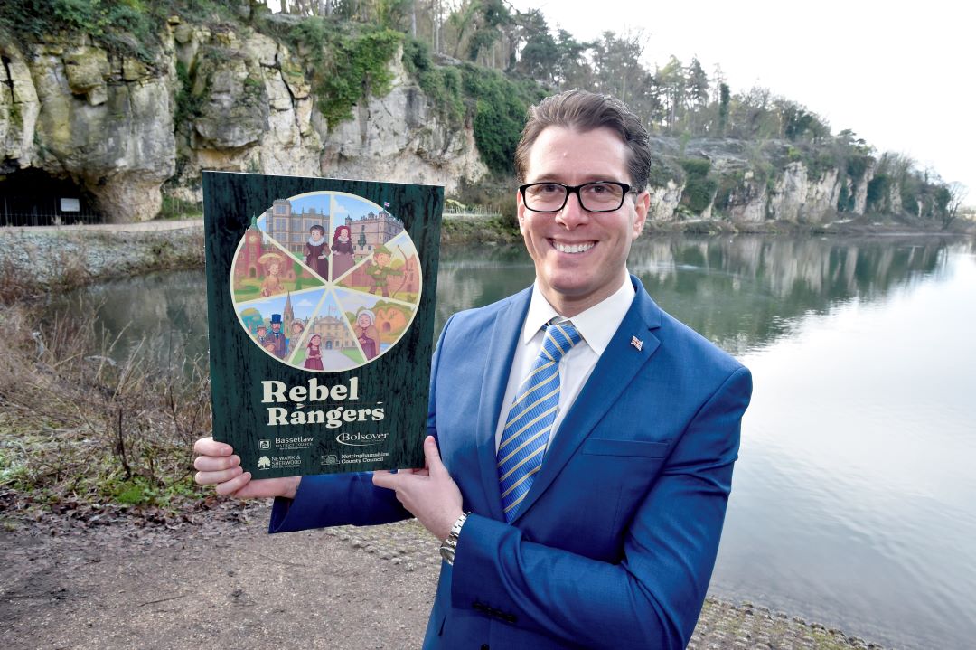 Councillor Walker-Gurley is holding up a plaque which features the rebel rangers branding, with the water and caves of Creswell Crags in the background  