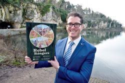 Councillor Walker-Gurley is holding up a plaque which features the rebel rangers branding, with the water and caves of Creswell Crags in the background  