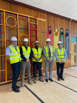Partners are lined up wearing hi-vis and hard hats.  In the background is the school hall 