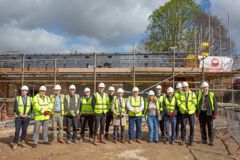 Councillors and partners are standing in front of the new building which is still under construction.  Everyone is wearing hard hat and hi-vis jackets 