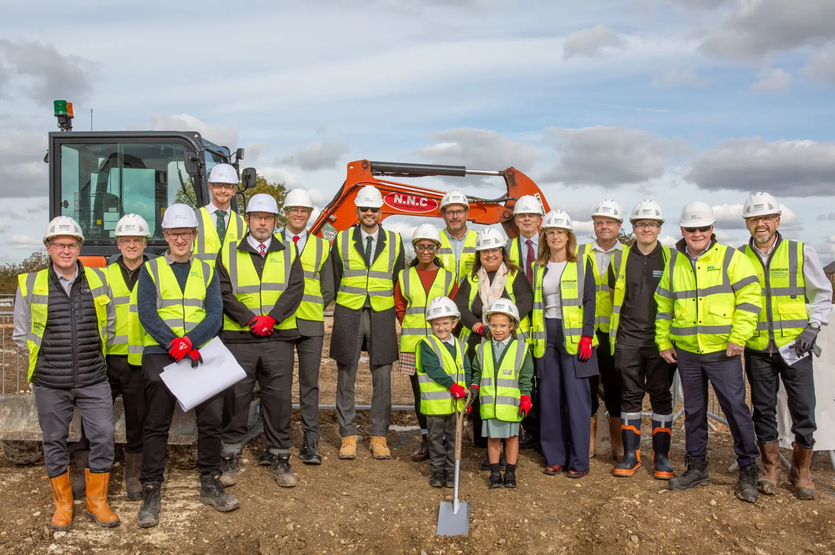 Councillor James Walker - Gerling and staff from Nottinghamshire County Council and Arc standing on the construction site of a new school with two children in front holding a spade. 