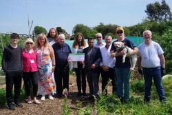 Councillors, volunteers at Jigsaw, are standing together in an allotment with councillors holding a giant cheque to demonstrate the amount of funding allocated 