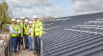 Councillor and partners are standing on a walkway by the side of the new building's roof. Everyone is wearing hard hats and hi-vis jackets