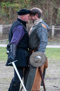 Two performers, one holding a sword, the other a shield, are squaring up to each other, with their foreheads touching 