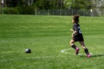 A young girl dressed in a football kit running towards a ball in a field.