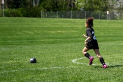 A young girl dressed in a football kit running towards a ball in a field.