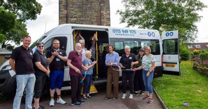 Volunteers, staff and members of the community are standing around the new minibus