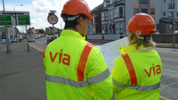 Two people wearing hi viz jackets with the Via logo on looking at drawings next to a road