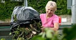 A woman emptying garden waste into a skip at a recycling centre